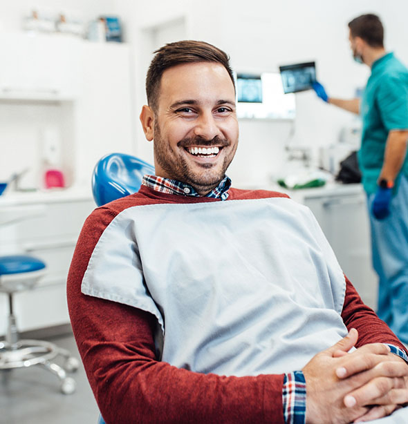 Man smiling confidently while sitting in a dental chair during a checkup.