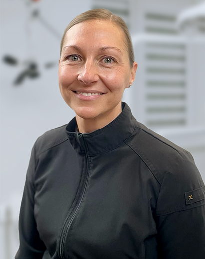 Dental hygienist in a dark jacket smiling in a dental clinic environment.