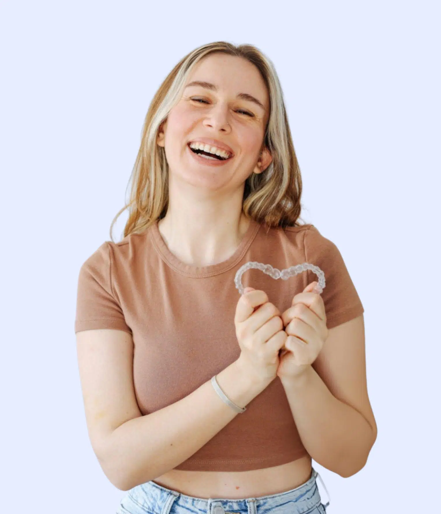 Smiling woman in brown shirt making heart shape with hands against light blue background