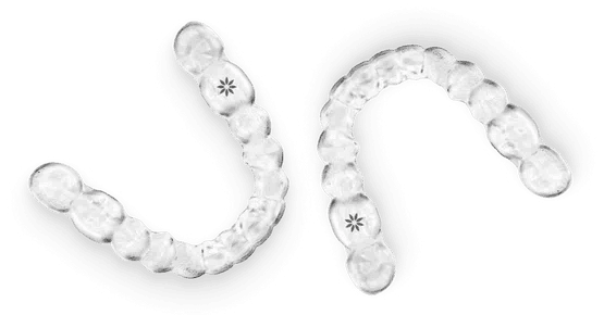 Clear plastic dental aligners with attachment dots arranged in curved rows on white background.