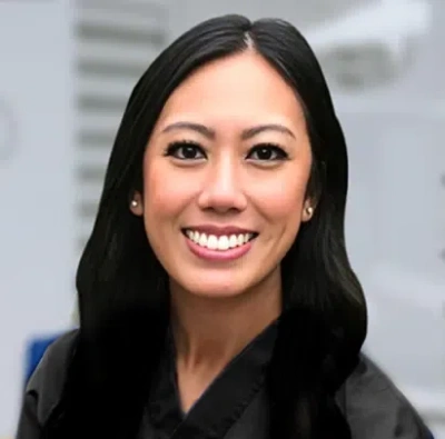 Professional headshot of smiling woman with long dark hair in dental office setting.