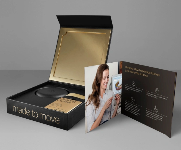 Black luxury dental box open displaying gold interior with patient brochure and information cards.